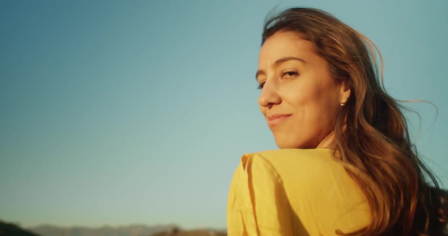 Woman wearing yellow walks toward hills on horizon under clear blue sky