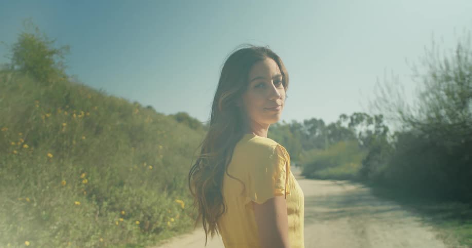 A young woman stands on a rural road and turns around and smiles