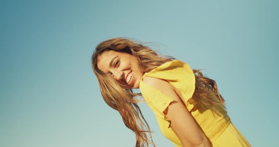 A woman in a yellow dress staring and smiling with the sky and clouds in the background