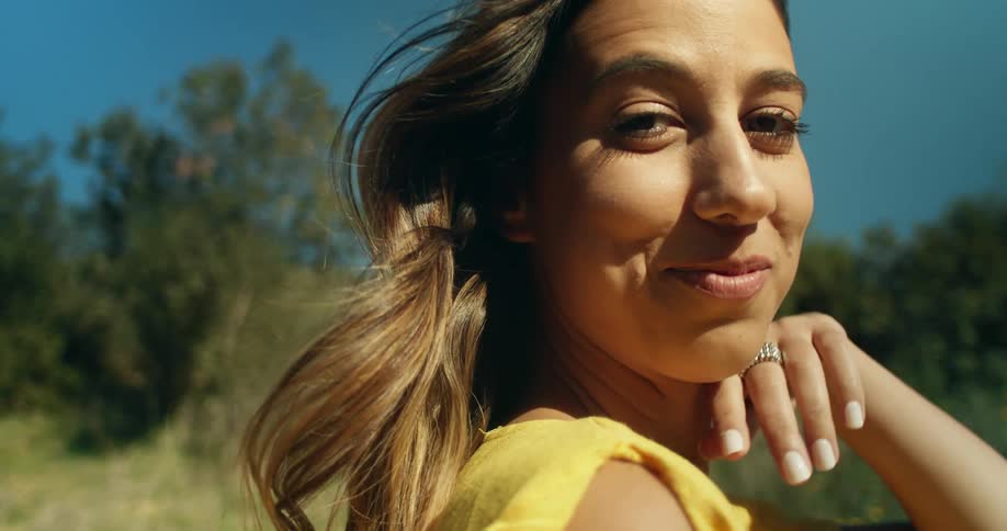 A young woman smiles into the camera while posing on a hill on a clear day