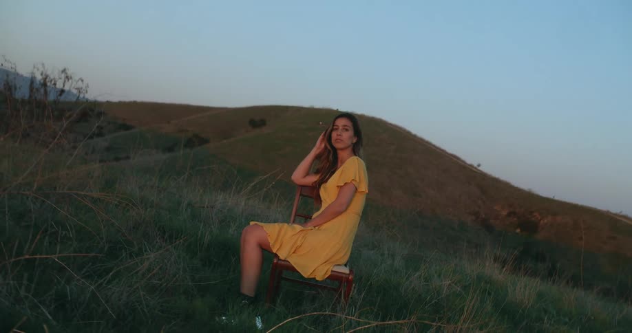 A woman in a brightly colored dress sits in a chair in a field and poses for the camera