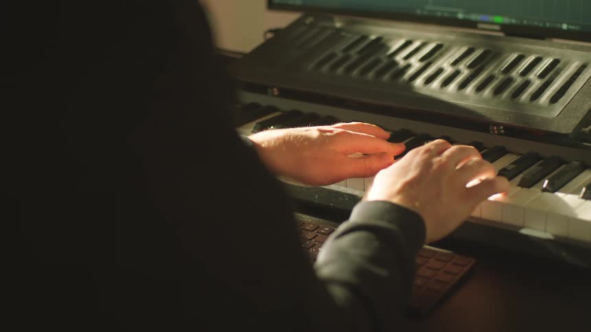 A person in a studio playing a keyboard with a monitor in the background
