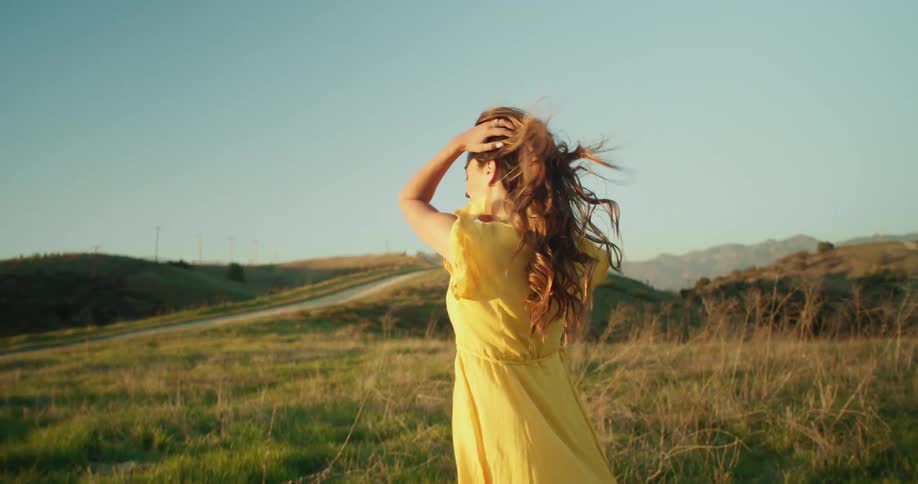 Woman with wavy brown hair and yellow dress wanders around the field