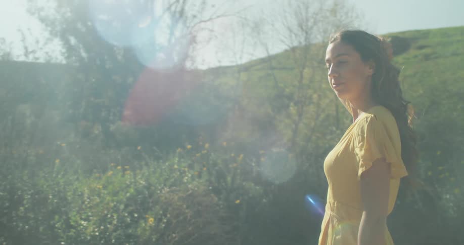 Woman wearing yellow smooths hair back walking at foot of hill on bright sunny day