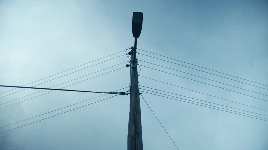 A street light with power lines attached to it under a cloudy daytime sky