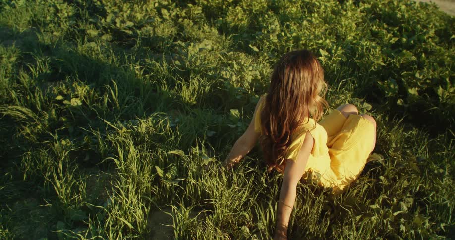 A woman in a yellow dress sits and relaxes in a grassy field