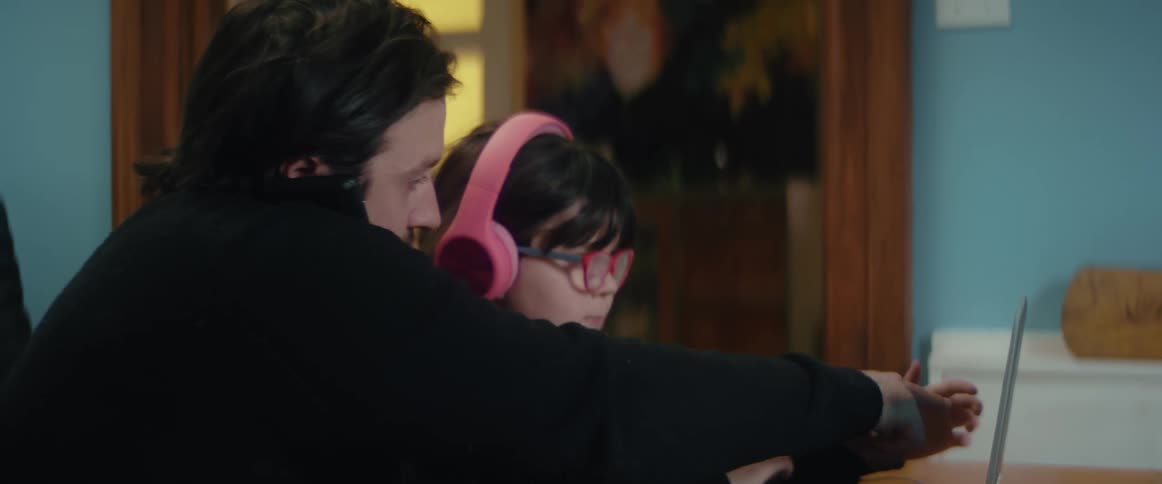 A man talks on his cell phone as he helps his daughter on her laptop