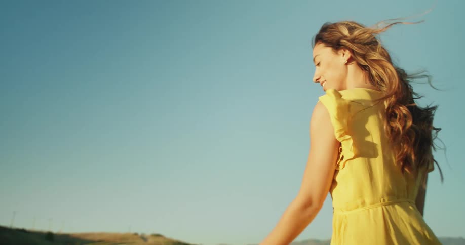 A female is waving her hands while wearing a yellow sundress