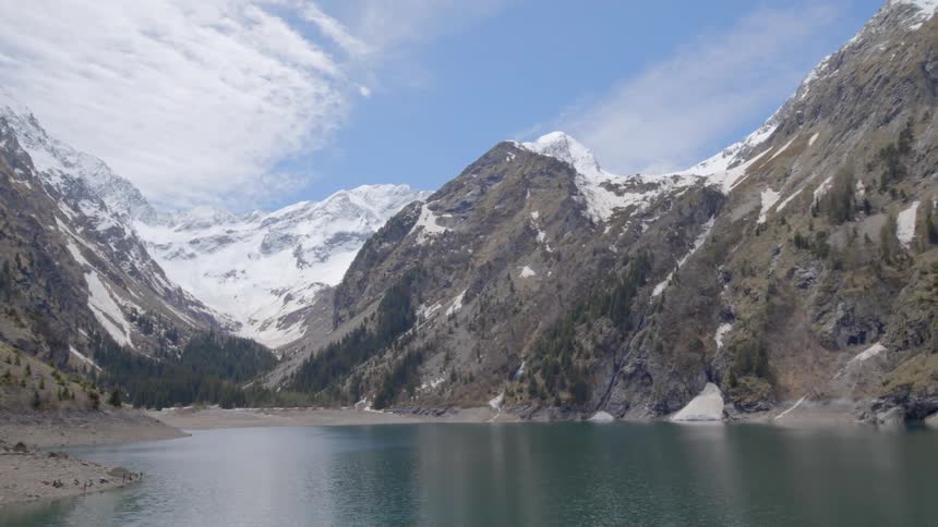 Calm lake at the base of a mountain range with tall peaks covered in snow