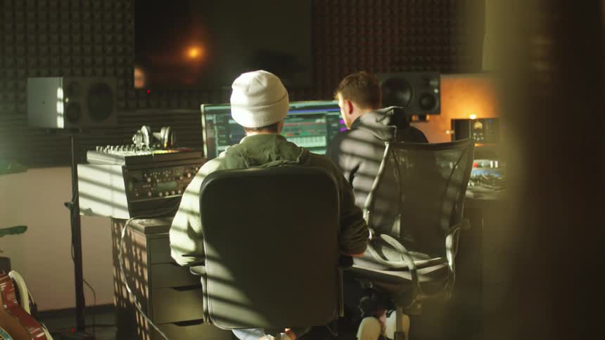 Two musicians recording and editing music in a computer inside a studio