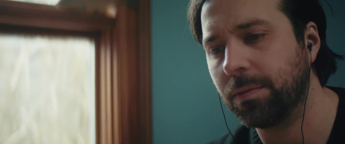 Bearded man wearing earbuds talking on a room at home