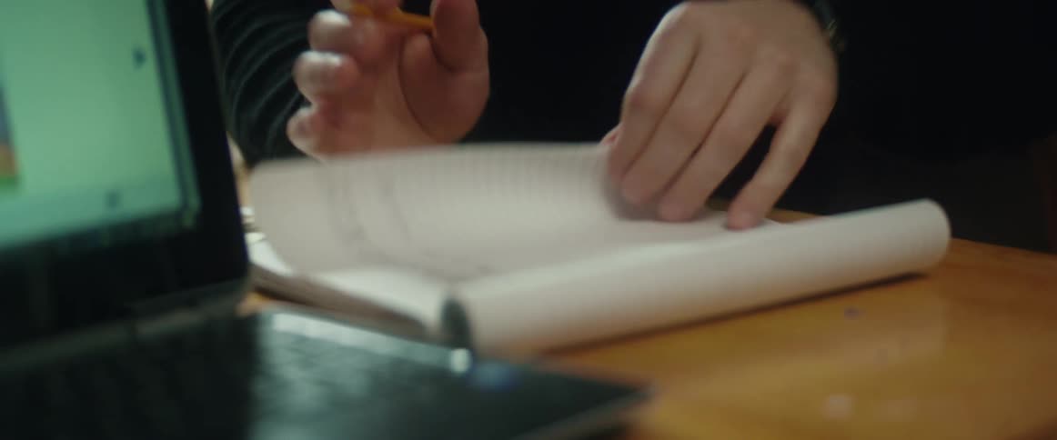 A man sighs as he flips his notebook and talks to a person sitting in front of a laptop