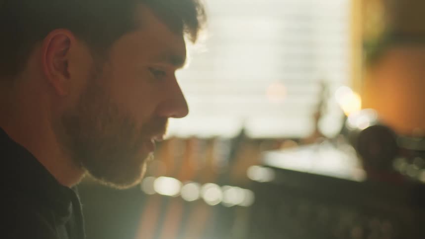 A bearded man sitting inside a music studio seems to be in deep thoughts