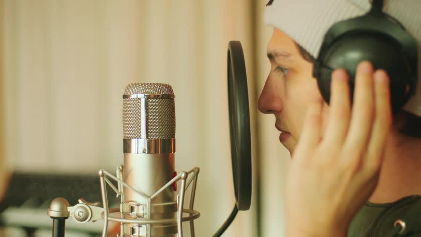A man in a room with headphones singing into a microphone with a pop guard