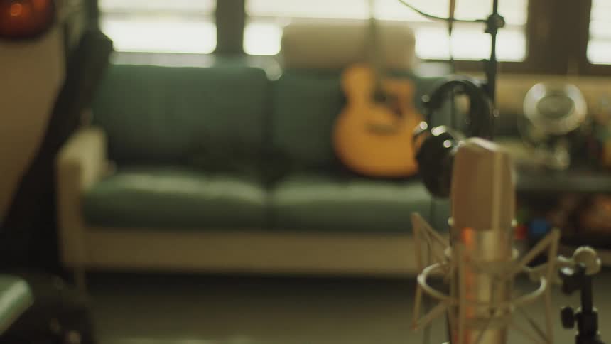 Close up of a professional microphone while a headphone and a guitar can be seen in the background
