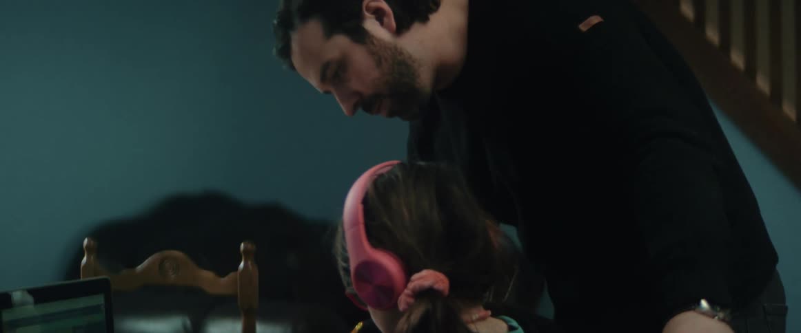 Father gets up from his laptop to help daughter working at dining table nearby on her laptop