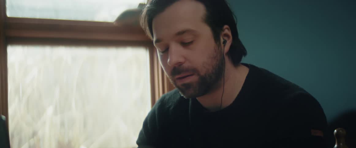 Man with beard and black sweater listens to music with earphones