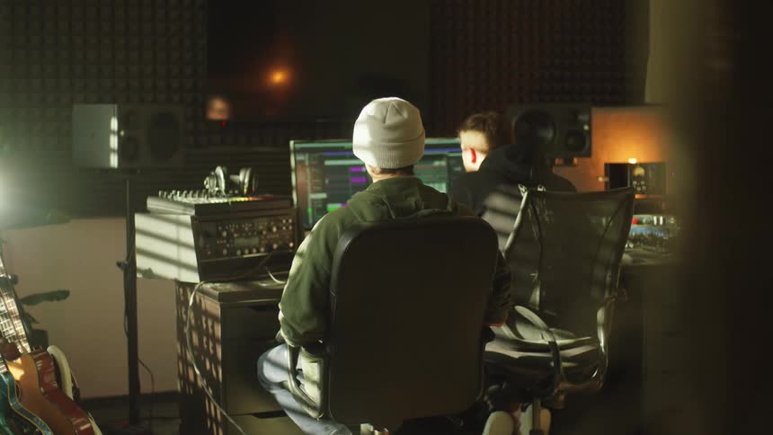 Two musicians editing music on a computer inside a studio