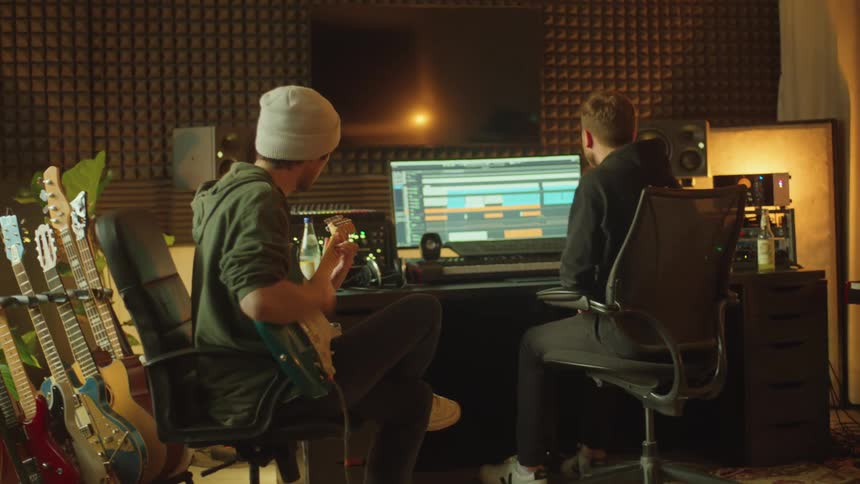 A man plays a guitar as another man records him