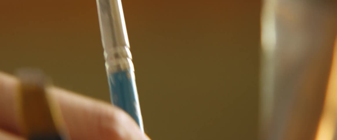 A hand picks up a paint brush that has paint on the bristles