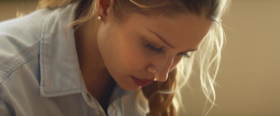 Blonde woman with nose piercing and light blue shirt looks down