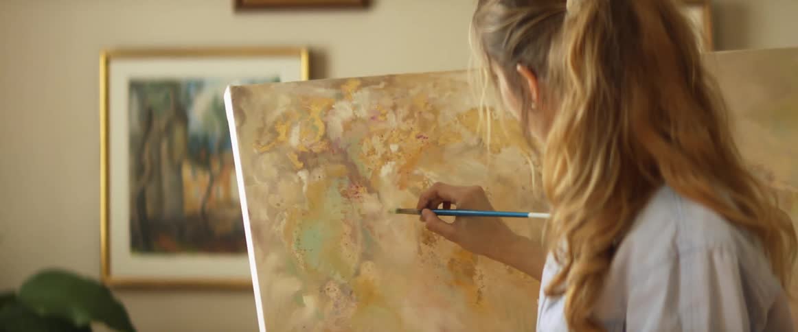 A woman blends together colors on a painting on a large canvas