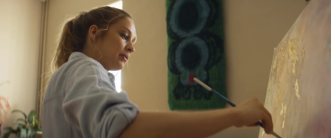 A woman brushes paint onto a canvas and steps back to look at it