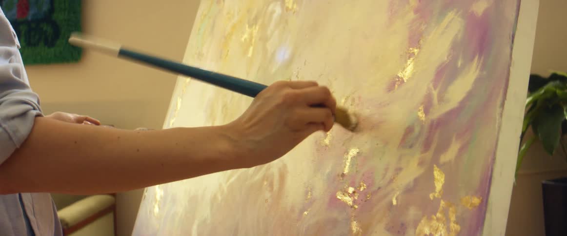 A painter uses white paint to blend an art piece on canvas