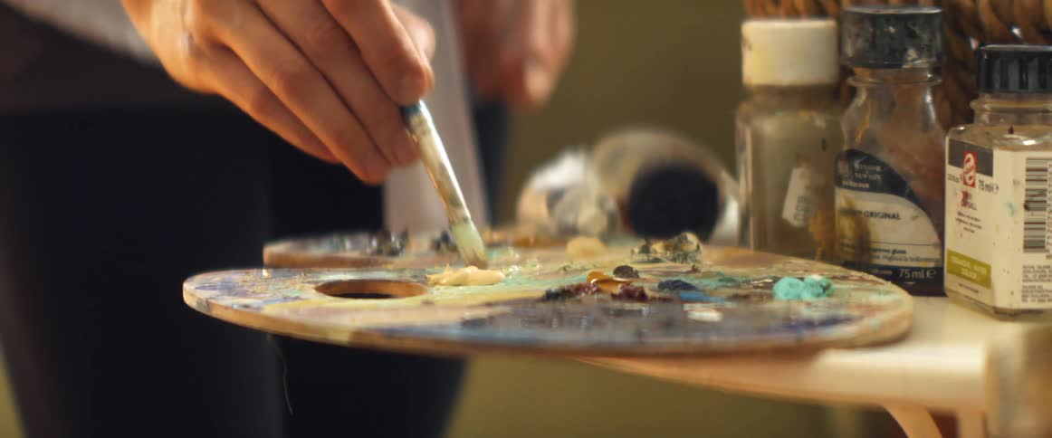 A woman blends paint by dabbing colors repeatedly on a palette