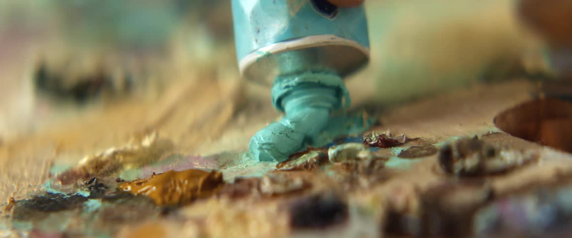 Hand squeezes turquoise paint out of oil paint tube