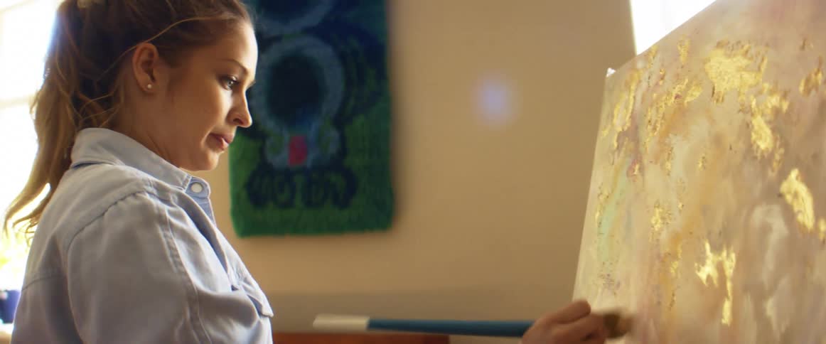 Woman paints on canvas in room with art on wall