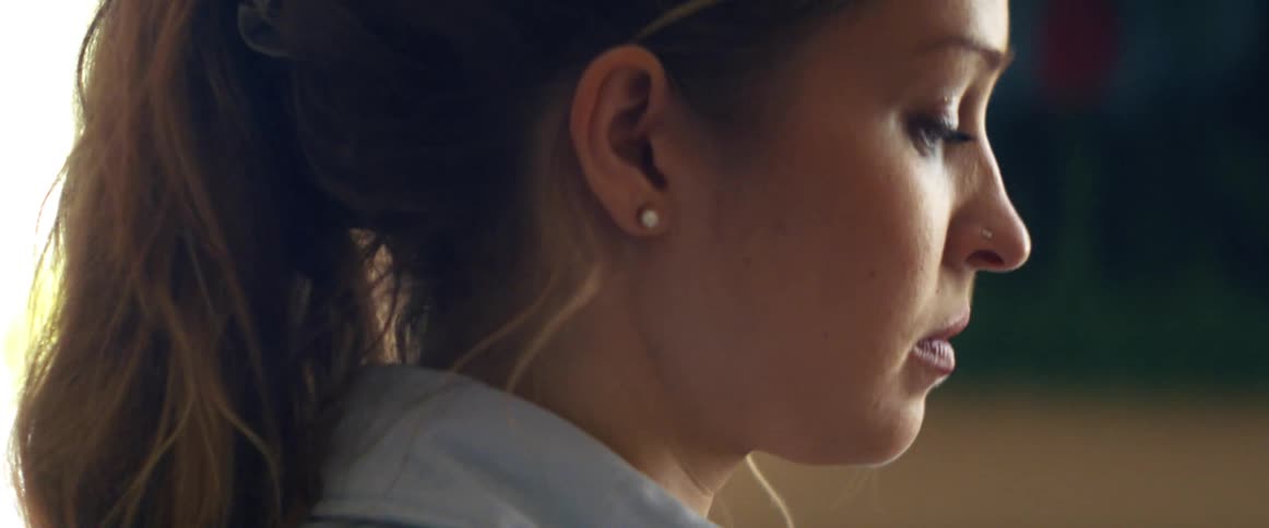 Woman wearing pearl earring and pony tail looks downward