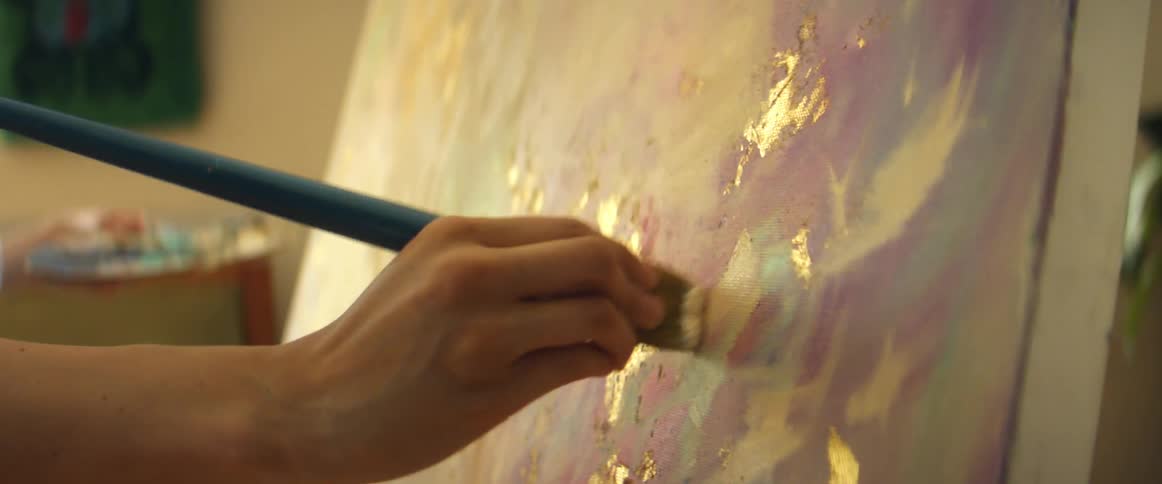 Female painter with light blue shirt paints on canvas