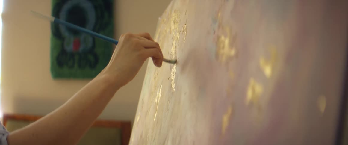 Artist dabs paint onto canvas full of pastels with golden pops of color