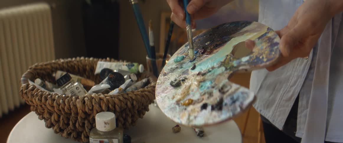 A woman blends pastel paints on a palette while painting at home