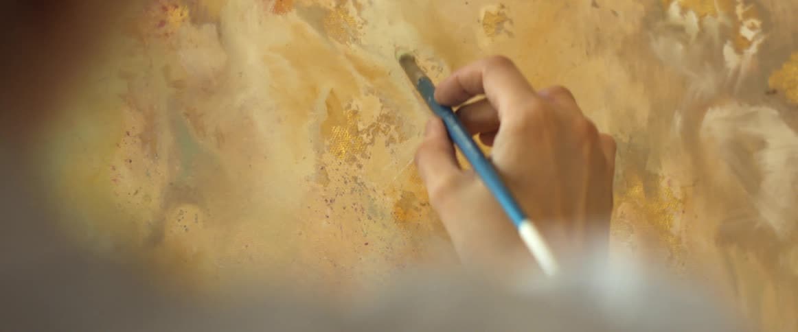 A woman blends yellow paint on a nearly finished art piece on canvas