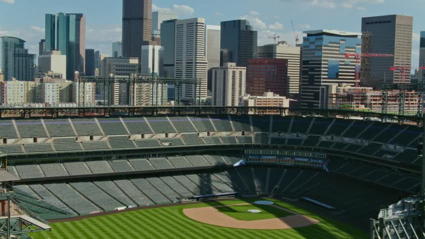 A baseball stadium with buildings the sky and clouds in the background