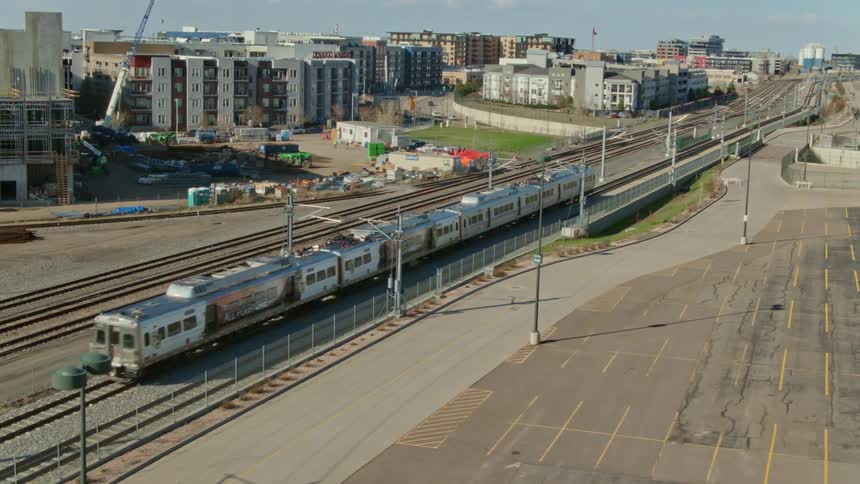 A train running on train tracks with buildings the sky and clouds in the background