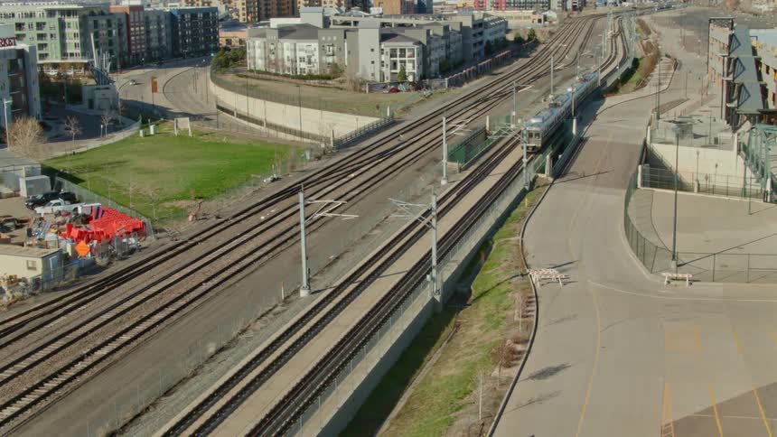 A train running on train tracks with buildings the sky and clouds in the background