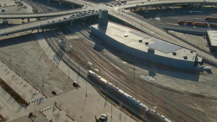 Train heads toward overpass as cars wait at stop light on raised freeway