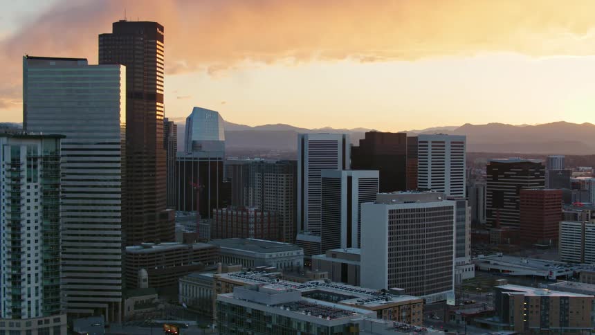 Sun sitting on horizon colors sky and clouds red and orange over mountains behind city downtown