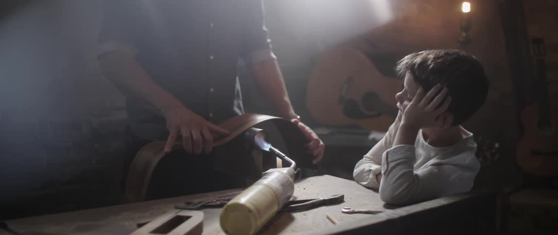 A boy watches someone making a guitar