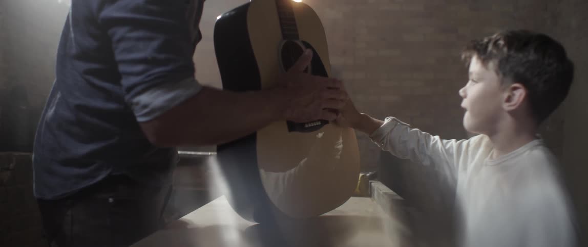 A man holds a guitar and a boy tap it together