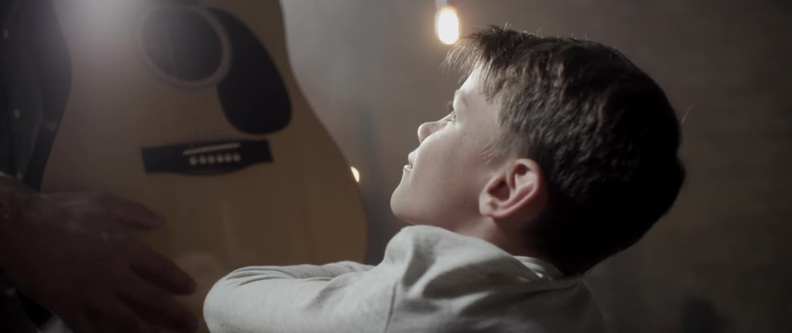 Boy looking up towards a guitar that a man is holding in front of him