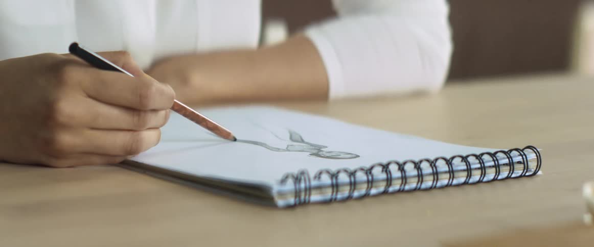 A woman sketches a woman in a dress in a notepad