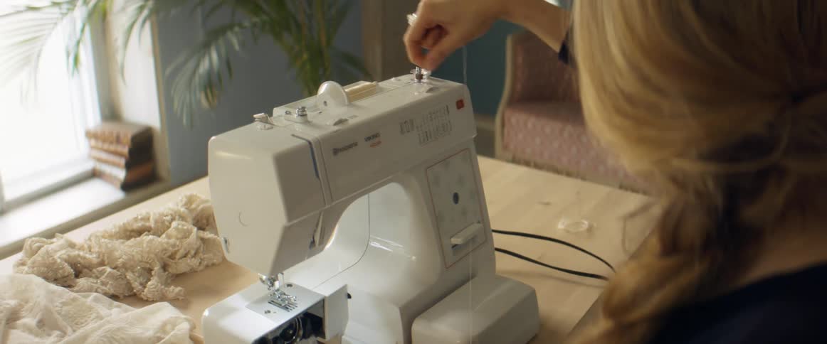 A woman threads a sewing machine in her home studio