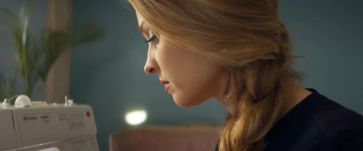 Young blonde woman uses a sewing machine inside a room