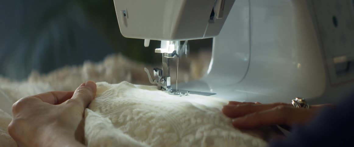 A person in a room using a sewing machine on a fabric