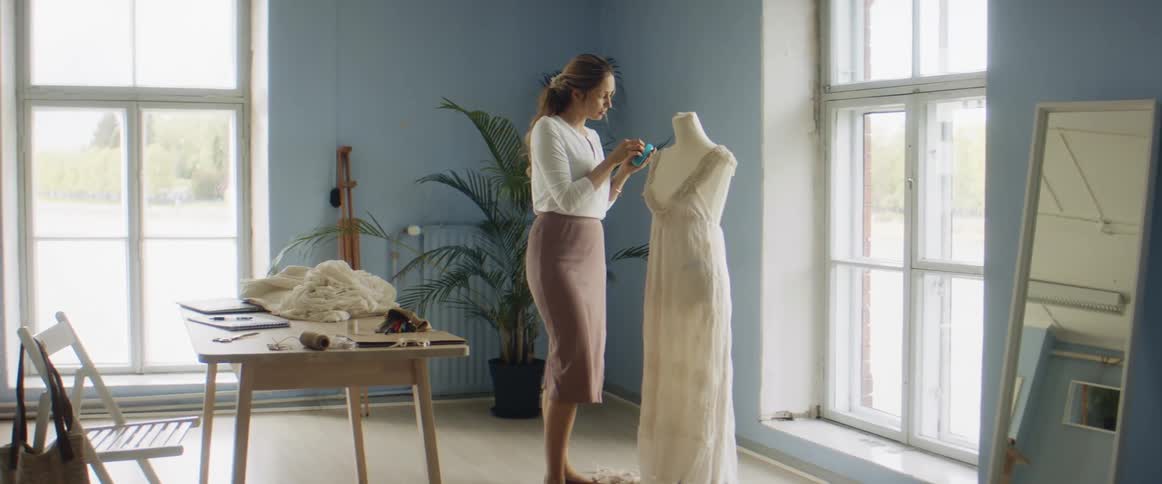 Young blonde fashion designer tailoring a dress over a mannequin on her studio