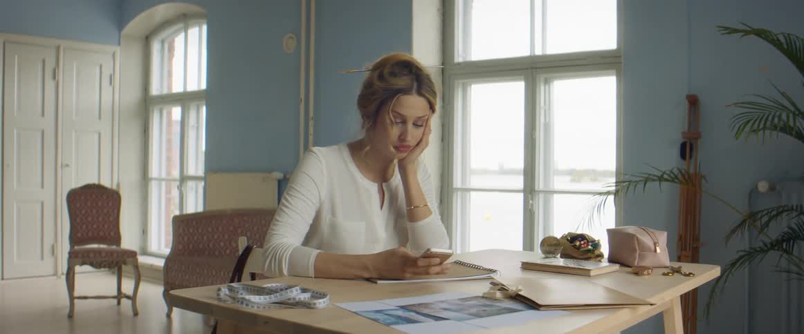 Woman sitting at wooden table stops working to look through mobile phone